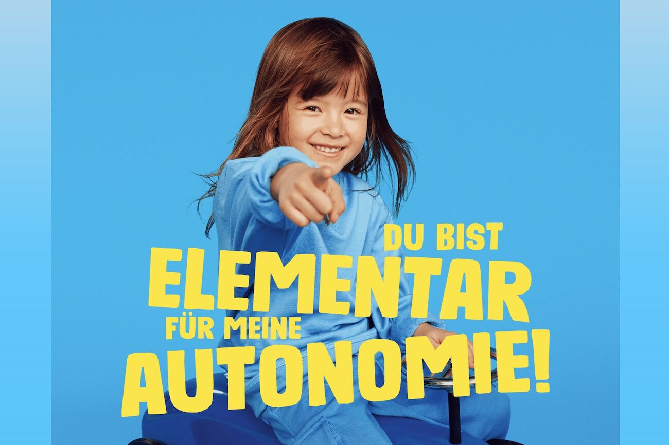 Ein Kind mit roten Haaren und blauem Pullover zeigt mit dem Finger nach vorne.