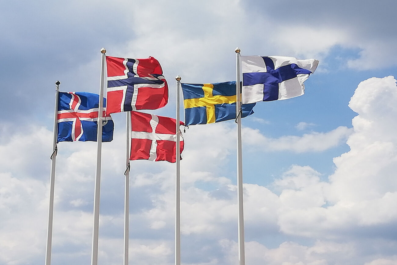 Fünf nordische Länderflaggen auf Masten vor einem bewölkten Himmel.