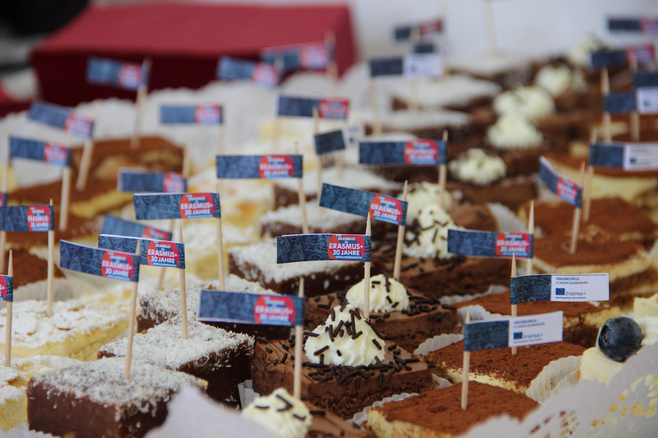 Verschiedene Kuchen mit kleinen Fähnchen oben drauf, dicht an dicht auf einem Tisch angeordnet.