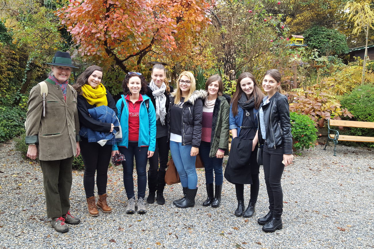 Eine Gruppe von acht Personen posiert im Freien in einem Garten mit Herbstlaub.