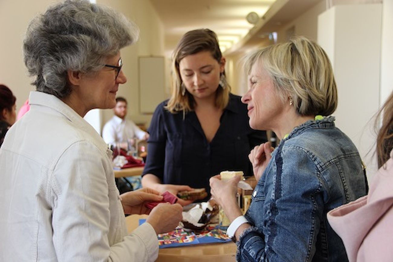 Drei Frauen unterhalten sich und essen gemeinsam bei einer gesellschaftlichen Veranstaltung im Innenbereich.