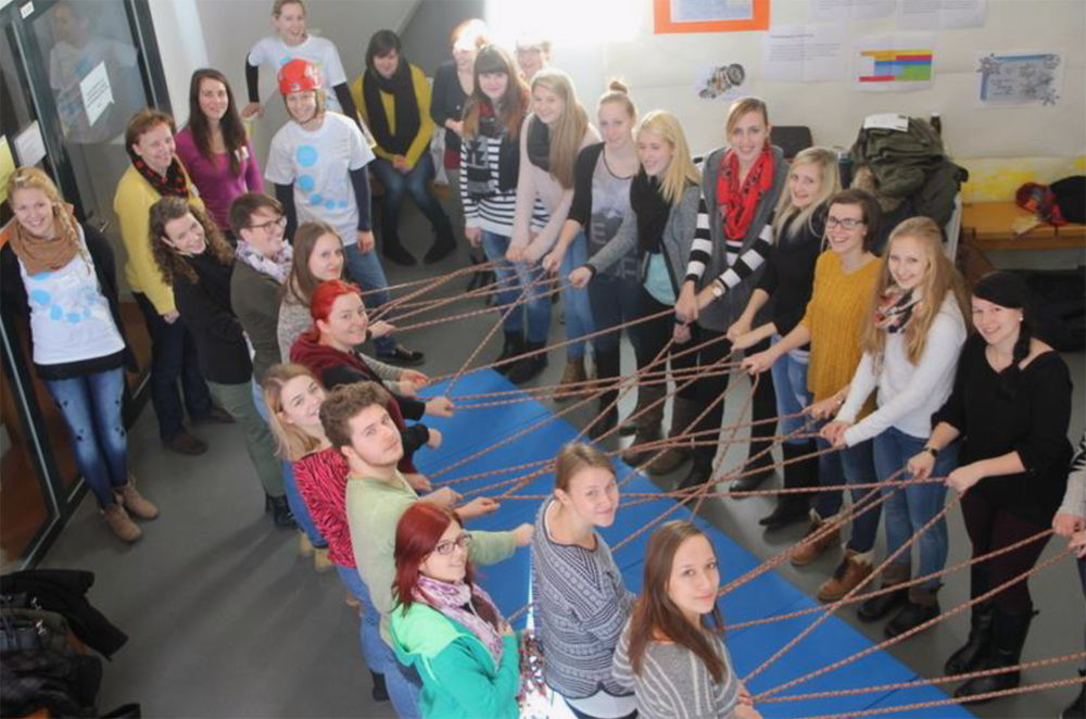 Eine Gruppe von Menschen steht im Rahmen einer Teambuilding-Aktivität mit Seilen in einem Kreis.