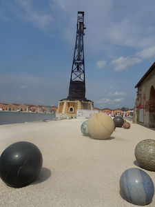 Großer Kran und bunte Steinkugeln an einer Uferpromenade unter einem teilweise bewölkten Himmel.