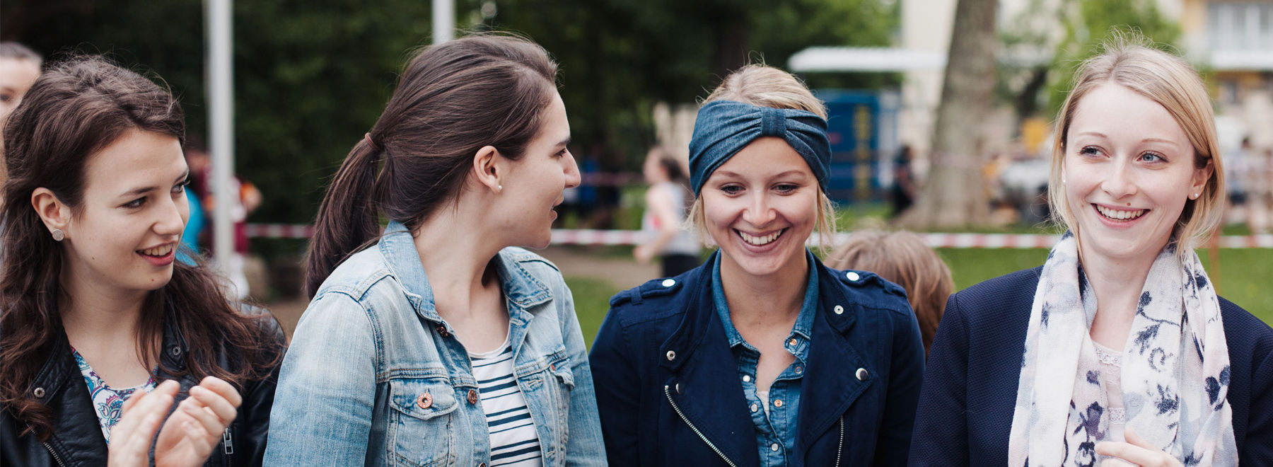 Vier junge Frauen lächeln und unterhalten sich an einem bewölkten Tag im Freien.