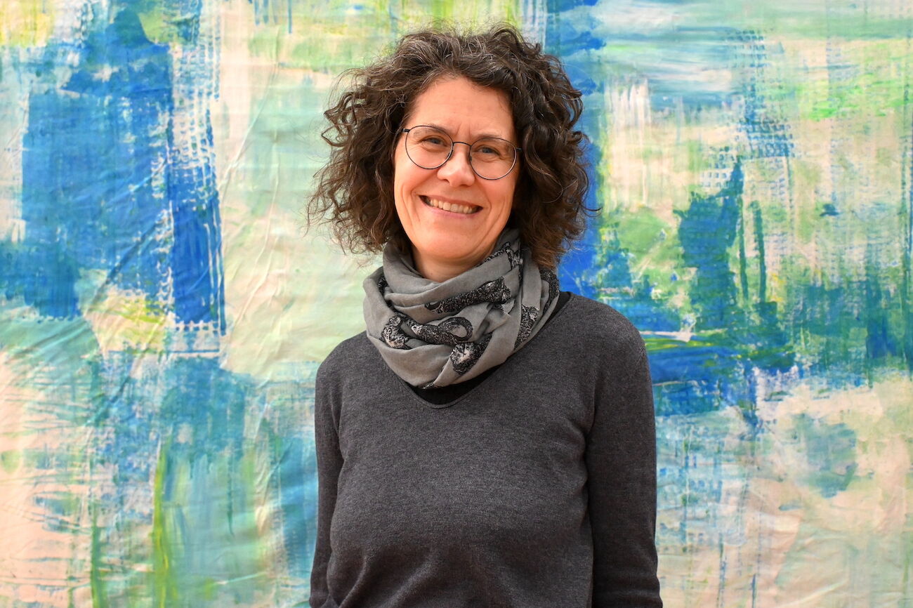 Frau mit lockigem Haar und Brille lächelt an einem Herbsttag im Freien.