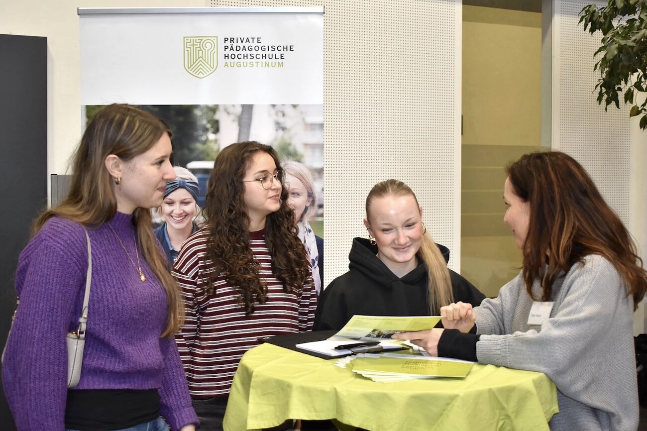Drei junge Frauen werden von einer Lehrperson im Foyer der Hochschule beraten.