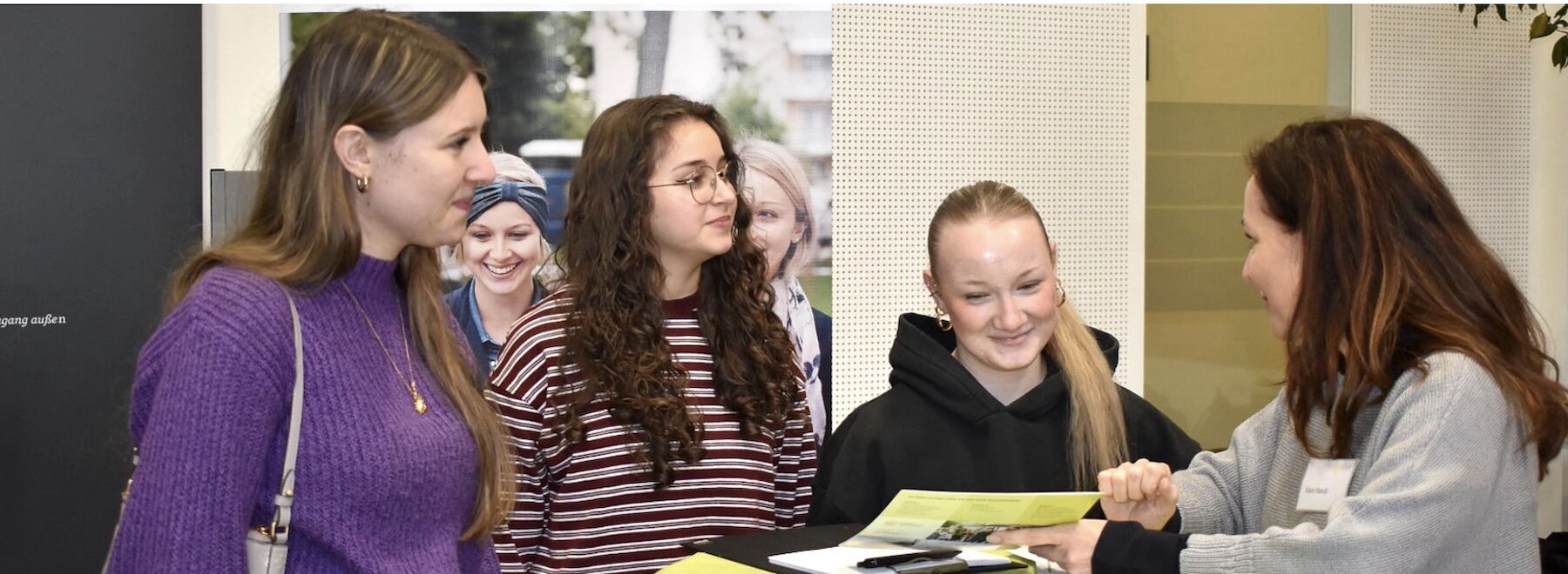 Drei junge Frauen werden von einer Lehrperson im Foyer der Hochschule beraten.