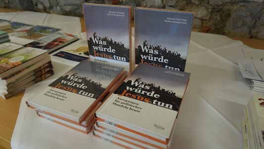 Stapel deutscher Bücher mit dem Titel „Was würde Jesus tun“ auf einem Tisch.