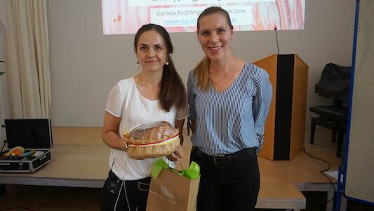Zwei Frauen lächeln; eine hält eine Geschenktüte und einen Korb mit Brot.