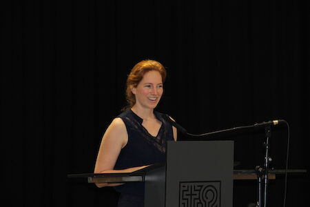 Eine Frau in einem marineblauen Kleid spricht an einem Podium mit einem Mikrofon.