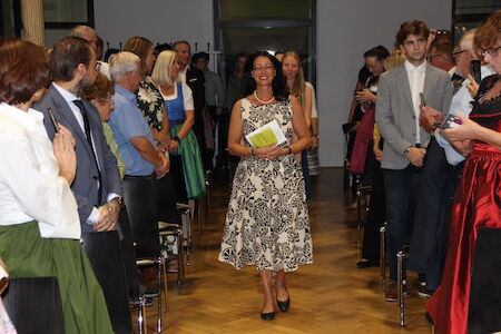 Eine Frau in einem geblümten Kleid geht einen Gang entlang, während die Leute auf beiden Seiten zuschauen.