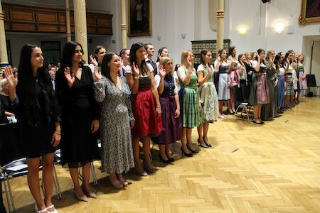 Eine Gruppe stehender Frauen hebt in einer formellen Zeremonie ihre rechte Hand.