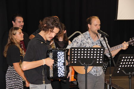 Eine Gruppe von Musikern tritt mit Gitarre, Akkordeon und Mikrofonen auf der Bühne auf.