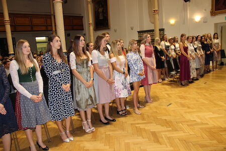 Eine Gruppe junger Frauen steht in halbformeller Kleidung in einem formellen Saal.