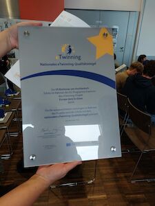 Eine Person hält in einem Klassenzimmer eine eTwinning-Auszeichnungsplakette.