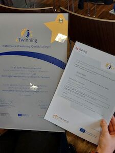 Eine Hand hält ein Zertifikat und ein Dokument mit dem eTwinning-Logo.