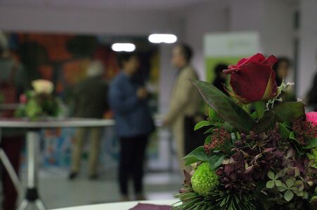 Nahaufnahme eines Blumenarrangements mit sich unterhaltenden Personen im unscharfen Hintergrund.