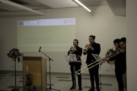Vier Musiker spielen Blechblasinstrumente neben einem Podium in einer modernen Inneneinrichtung.