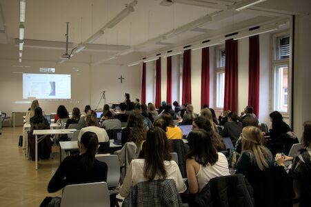 Die Schüler sitzen in einem Klassenzimmer und sehen sich eine auf eine Leinwand projizierte Präsentation an.