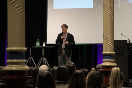 Mann hält vor Publikum in einem Hörsaal eine Präsentation.