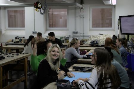 Schüler sitzen an Werkbänken in einem Klassenzimmer, unterhalten sich und lächeln.