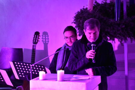 Zwei Männer sprechen an einem Podium mit Kerzen, das von violettem Licht erhellt wird.