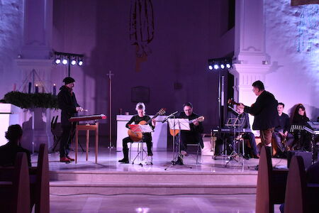 Musiker treten auf der Bühne in einer schwach beleuchteten Kirche mit violetter Beleuchtung auf.