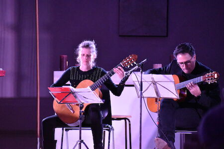 Zwei Personen spielen auf der Bühne klassische Gitarre und haben Notenblätter vor sich.
