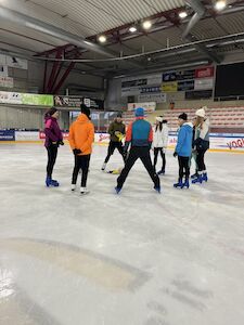 Eine Gruppe von Menschen läuft drinnen Schlittschuh und hat sich auf einer Eisbahn im Kreis versammelt.