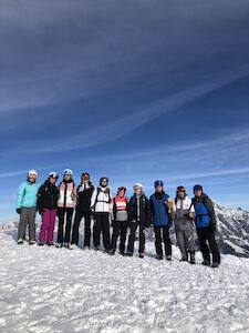 Eine Gruppe Skifahrer steht gemeinsam auf einem schneebedeckten Berg unter blauem Himmel.