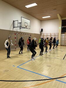 Eine Gruppe von Menschen tanzt in einer Turnhalle in der Nähe eines Basketballkorbs.