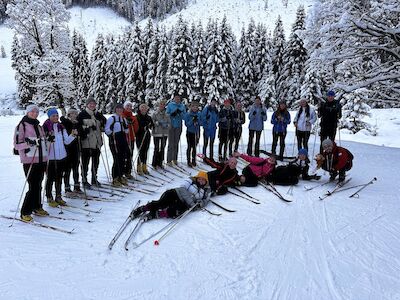 Eine Gruppe Skifahrer posiert gemeinsam auf einem schneebedeckten Hang mit Bäumen im Hintergrund.