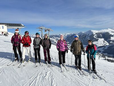 Eine Gruppe von sechs Skifahrern posiert mit Skistöcken auf einem schneebedeckten Berghang.