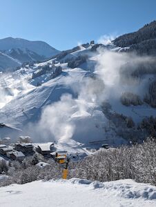 Schneebedeckter Berg mit Schneemaschinen, die unter blauem Himmel Pulverschnee auf die Skipisten blasen.