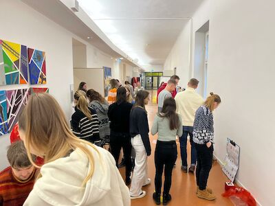 Eine Gruppe von Menschen versammelt sich in einem hellen Flur und schaut sich die Schaustücke an der Wand an.