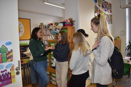Vier junge Frauen unterhalten sich mit einer Lehrerin in einem farbenfrohen, schön dekorierten Klassenzimmer.