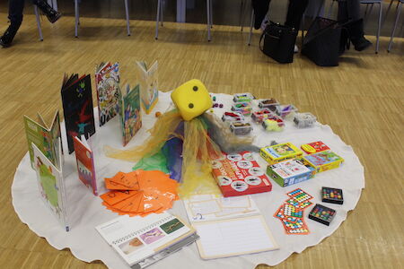Kinderbücher, Spiele und Bastelsachen sind auf einem runden Tuch auf dem Boden angeordnet.