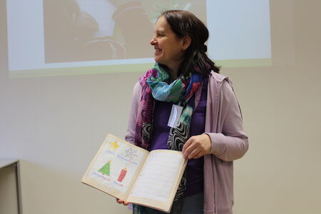 Eine Frau lächelt und hält ein offenes Notizbuch mit bunten Zeichnungen und Schriften in der Hand.