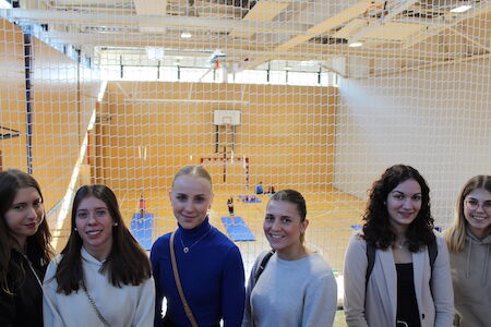 Sechs junge Frauen stehen vor einem Netz in einer Sporthalle.