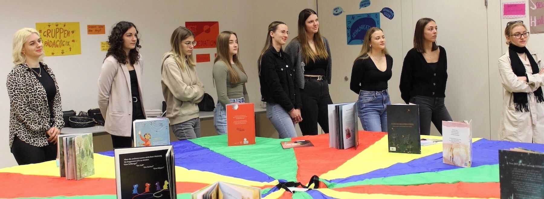 Neun Frauen stehen um einen bunten Tisch, auf dem Bücher ausgestellt sind.