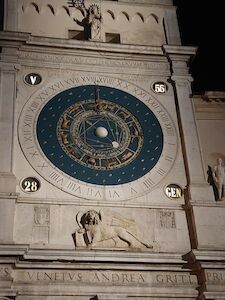 Astronomische Uhr mit römischen Ziffern auf einem Steingebäude bei Nacht.