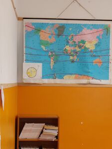 Eine Weltkarte an einer Wand über einem Regal mit gestapelten Papieren und Büchern.