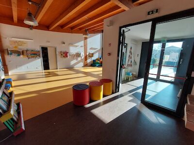 Ein heller, leerer Klassenraum, durch dessen große Fenster Sonnenlicht strömt.