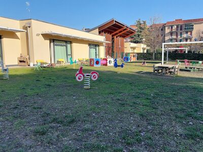 Spielplatz mit Federwippen, Gras und Gebäuden im Hintergrund an einem sonnigen Tag.