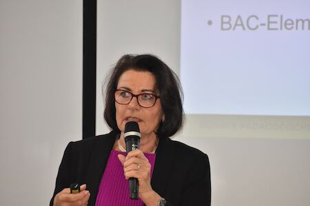 Frau mit Brille spricht während einer Präsentation in ein Mikrofon.