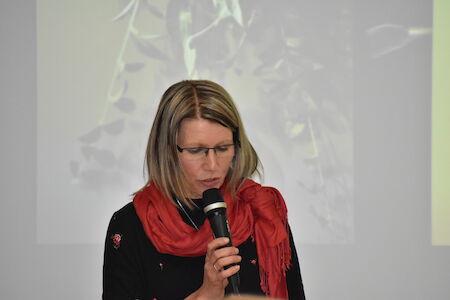 Frau mit Brille und rotem Schal spricht im Innenbereich in ein Mikrofon.