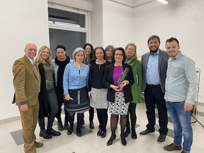 Elf Erwachsene stehen zusammen und lächeln für ein Gruppenfoto in einem Innenbereich.