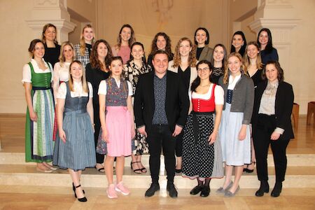 Eine Gruppe von Frauen und ein Mann posieren auf Stufen, viele tragen traditionelle Kleidung.