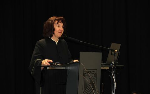 Eine Frau spricht an einem Podium mit einem Mikrofon und einem Laptop vor sich.