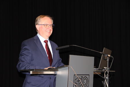 Ein Mann im Anzug spricht an einem Podium mit Laptop und Mikrofon.